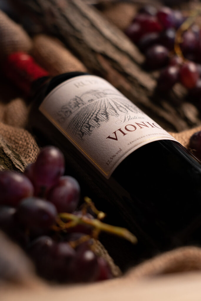 Productfoto van fles Rode wijn van Rubis, aangekleed met rode druiven en houten structuren.